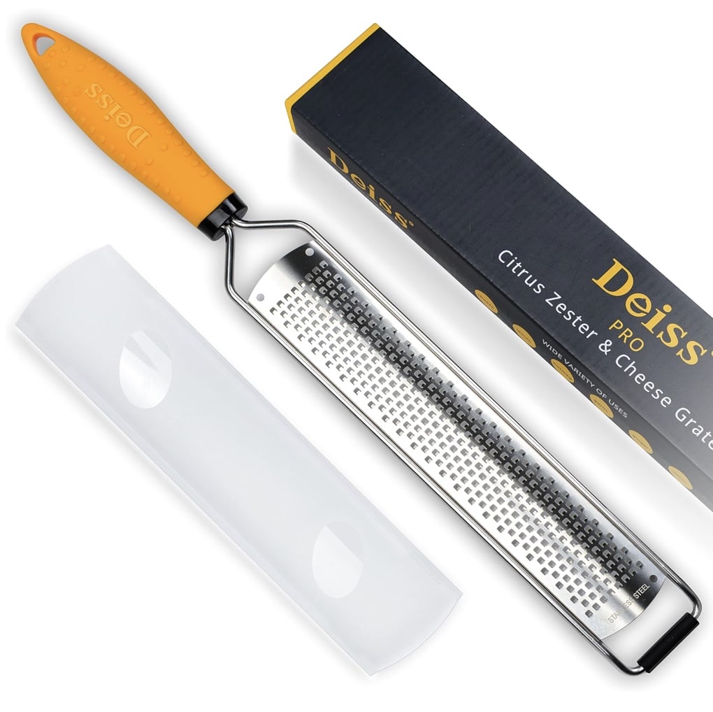 A Deiss PRO citrus zester and cheese grater with a bright orange handle sits next to its black and yellow box, ready to help you craft the perfect healthy lemon loaf recipe. A protective plastic cover is also visible, promising safe storage.